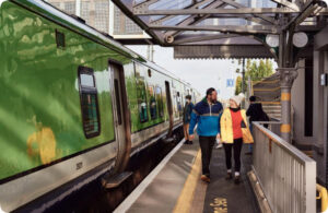 Passengers walking along a train platform beside a green commuter train at a station.