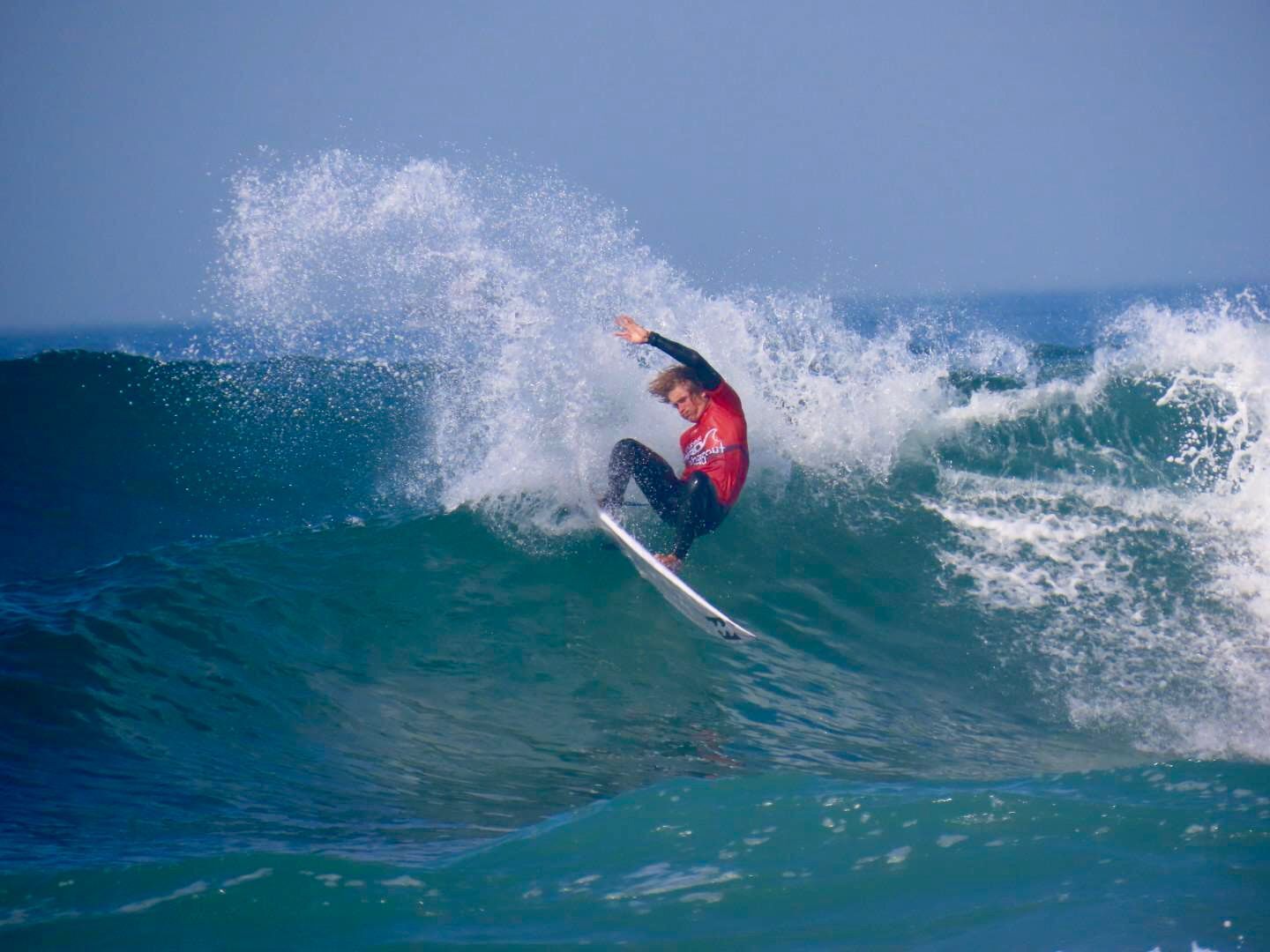 Surfer performing a sharp turn on a breaking wave, creating a dramatic spray of water in the open sea.